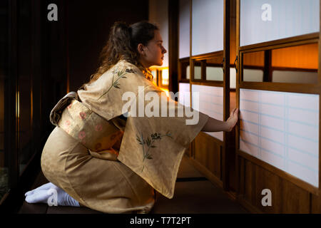 Casa tradizionale giapponese o ryokan con pavimento in tatami pavimento e gaijin donna in kimono e dei tabi calzini apertura porte scorrevoli di carta shoji Foto Stock