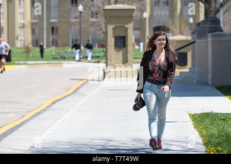 Lexington, Stati Uniti d'America - 18 Aprile 2018: giovane donna sorridente, fotografo professionista con fotocamera DSLR camminando sul marciapiede sul campus della Virginia Mil Foto Stock