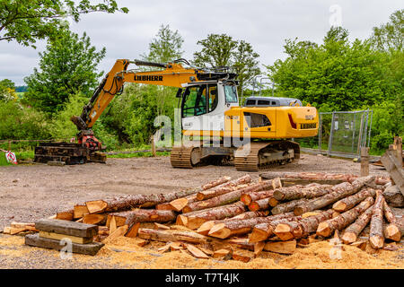 Escavatore Liebherr digger utilizzato per la registrazione o la raccolta di legname, con log in primo piano. Northumberland, Regno Unito. Maggio 2018. Foto Stock