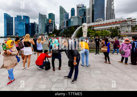 I turisti che posano per una foto davanti alla statua Merlion e dello skyline di Singapore, Singapore, Sud-est asiatico Foto Stock