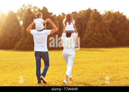 Vista da dietro. Una famiglia con bambini stanno camminando sul prato di un parco . Foto Stock