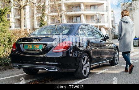 Strasburgo, Francia - Feb 23, 2017: Moda donna spensierata camminando verso il lusso di Mercedes-Benz E220d diesel auto parcheggiata su una strada tranquilla nella città francese Foto Stock