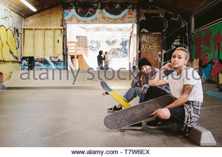 Ritratto fiduciosi, fresco giovane femmina skateboarders a indoor skate park