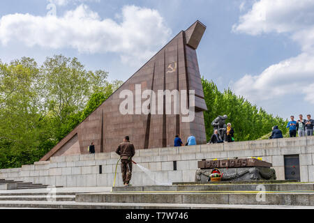 Statua di un soldato sovietico inginocchiato di fronte a una bandiera sovietica stilizzata costruita da granito rosso al Memoriale di guerra sovietico a Treptow, Berlino, Germania Foto Stock