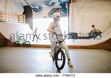 Madre su bmx bike a guardare i bambini giocare sulla rampa a indoor skate park
