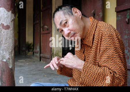 Agente Orange vittima Minh Nguyen lungo (64 anni) si siede su uno sgabello davanti a suo figlio home. L'unità PHU Ly village (Ha Nam provincia) vicino a Hanoi, Vietnam Foto Stock