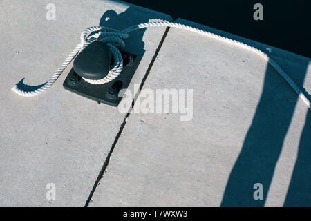 Ormeggio yacht corda con una estremità annodata legato attorno un gancio su un molo di cemento. Con ombre profonde e spazio di copia Foto Stock