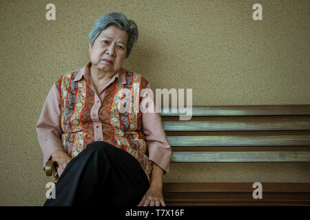 Annoiato premuto asian elder donna seduta sul banco. anziani sensazione femmina triste lonely. senior lifestyle Foto Stock