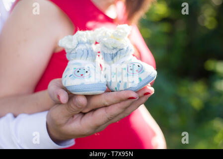 Incinta giovane azienda lavorate a maglia blu e bianco babbucce sullo sfondo della pancia Foto Stock