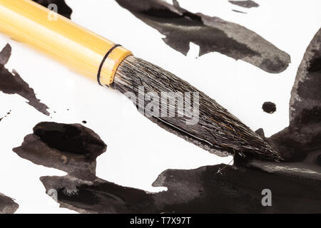 Tinto nero round pelo di capra punta del pennello di bambù per sumi-e ( suibokuga) pittura su macchie di inchiostro sulla carta bianca close up Foto Stock