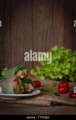 Insalata rotoli sulla piastra bianca collocata su una sacca vi è il pomodoro e il peperoncino collocato accanto e lattuga collocati sul lato posteriore. Foto Stock