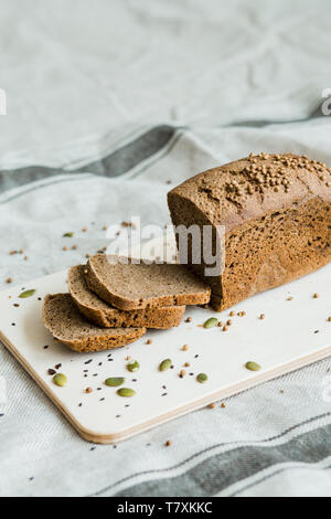 Pane appena sfornato a fette di pane su una tavola di legno sul grigio scuro tessuto con sementi Foto Stock