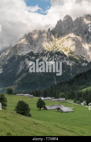 Vista rurale dalle Alpi Svizzere, intorno a Grindelwald, con picchi rocciosi avvolte in nuvole in background e verdi pascoli con le aziende agricole in foregr Foto Stock