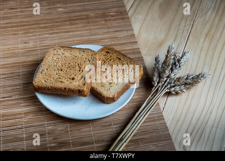 Due fette di pane tostato e orecchio di grano su un tavolo di legno Setup Foto Stock