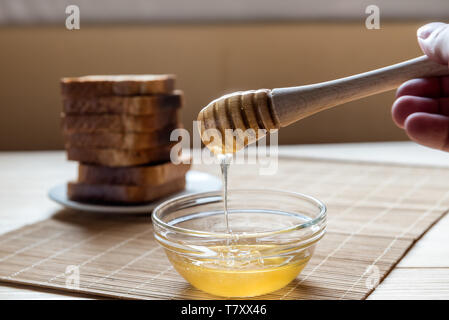 Un vasetto di miele con miele il bilanciere con pane tostato in background su un tavolo di legno Setup Foto Stock