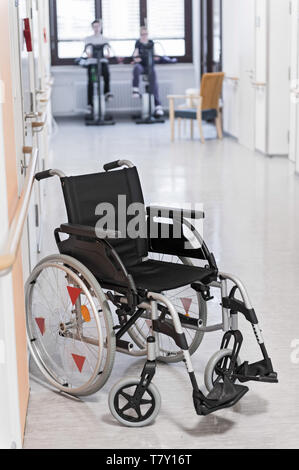 Un vuoto che la sedia a rotelle si erge di fronte due biciclette dispositivi di formazione con i pazienti. Foto Stock