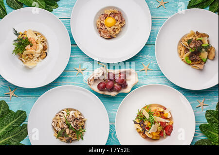 Set di pasta in blu sullo sfondo di legno. cucina italiana laici piana. Il cibo gourmet. Delizioso ristorante piatti. Foto Stock