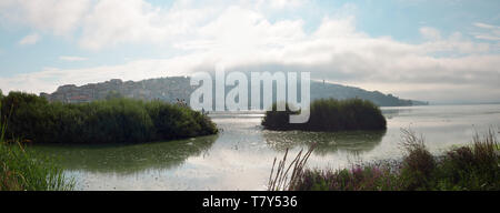 Cielo nuvoloso e il sole entra attraverso le nuvole sopra la città e il lago in una mattina di primavera Foto Stock