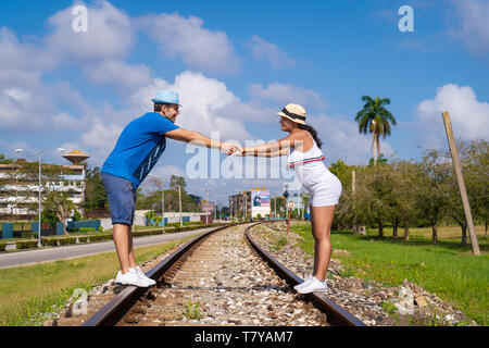 Coppia di giovani indossano hat detenute dalle loro mani permanente sulla linea ferroviaria, un cielo con alcune nuvole in background Foto Stock