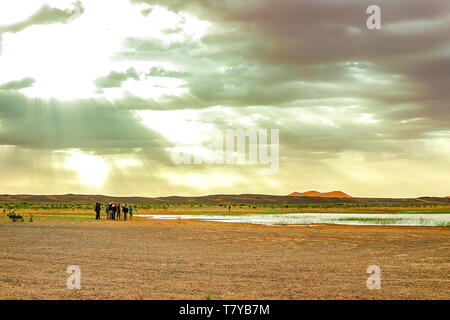 Il lago in Marocco all'alba ai piedi del deserto del Sahara. Il sole splende attraverso le nuvole. Nel telaio della macchina e un gruppo di turisti che Foto Stock
