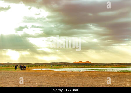 Il lago in Marocco all'alba ai piedi del deserto del Sahara. Il sole splende attraverso le nuvole. Nel telaio della macchina e un gruppo di turisti che Foto Stock