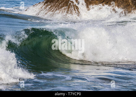 Blu-verdi wave curling come esso si rompe proprio offshore in Leo Carrillo State Park, California del Sud. Rocce costiere in background. Foto Stock