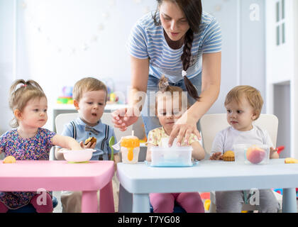 Un gruppo di bambini di vivaio i bimbi a mangiare cibo sano pausa pranzo insieme con kindergartener Foto Stock
