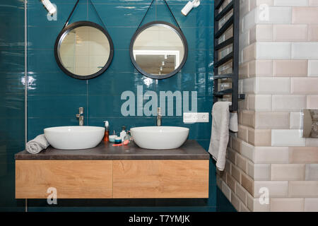 Moderno bagno interno con un ripiano in legno, due lavandini in piedi su di esso e round specchi. In vetro trasparente di cabina doccia, minimalista scandinavo Foto Stock