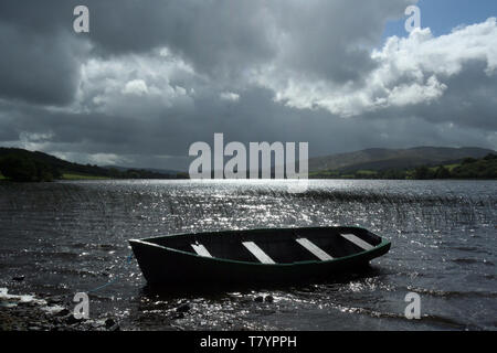 Una solitaria barca a remi si siede sulle calme acque di un lago con le montagne sullo sfondo in Gartan in Co. Donegal, Irlanda . Foto Stock