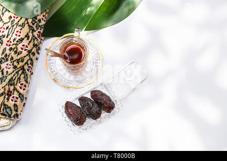 Il Ramadan concetto e l'ispirazione che mostra 3 palme da dattero in una crystal clear vassoio con il set per il tè e il tappeto da preghiera su sfondo bianco Foto Stock