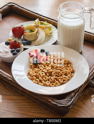 Una ciotola di cereali di avena su un vassoio di legno con un assortimento di frutta, yogurt e piccola brocca del latte. Vassoio di legno in corrispondenza di un angolo. Tenuta raccolto verticale. Foto Stock