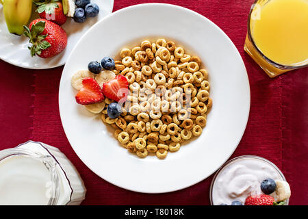 Scatto dall'alto di una ciotola di cereale con yogurt, un piatto di frutta fresca, brocca del latte e un bicchiere di succo di arancia come parte di una colazione bilanciata. Foto Stock