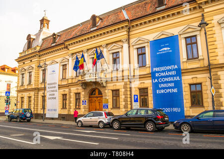 Sibiu, Romania - 22 Aprile 2019: Sibiu County prefettura (Institutia Prefectului Judetului Sibiu) vista esterna, con banner per la Presidenza romena Foto Stock