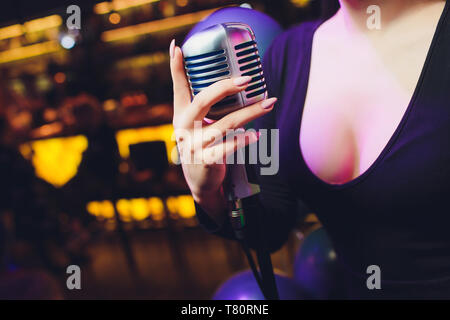 Femmina lato tenendo un singolo microfono retrò contro lo sfondo colorato Foto Stock