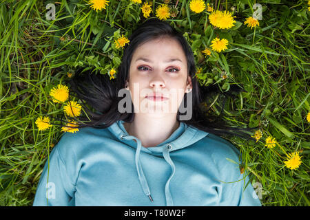 Testa e spalle Ritratto di giovane e bella donna sdraiata sul campo in erba verde e giallo di tarassaco, godersi la natura. La libertà e la natura Foto Stock