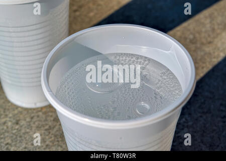 Bianco tazza in plastica a freddo con acqua minerale frizzante contro un bancone di pietra. Foto Stock