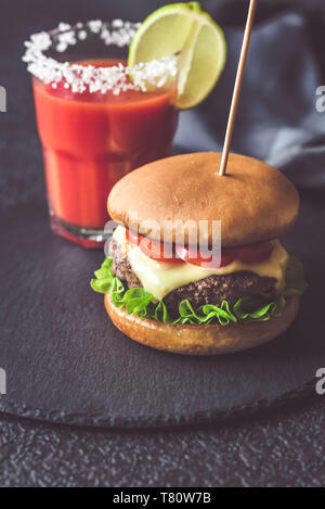 Hamburger con un bicchiere di succo di pomodoro sulla pietra nera board Foto Stock