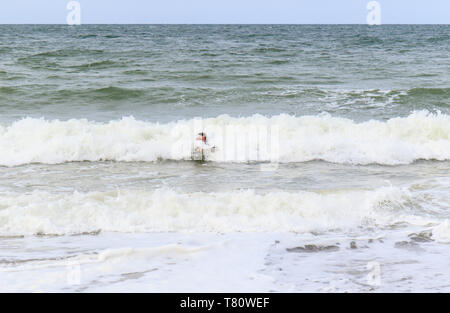 L'uomo surfboarding fuori della Costa North Norfolk, Regno Unito Foto Stock