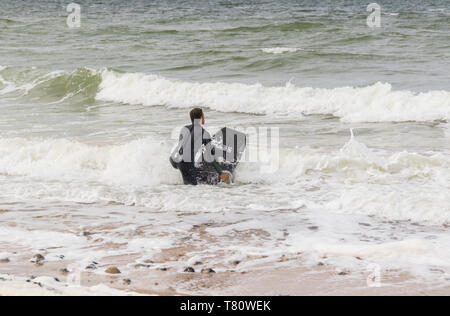 L'uomo surfboarding fuori della Costa North Norfolk, Regno Unito Foto Stock