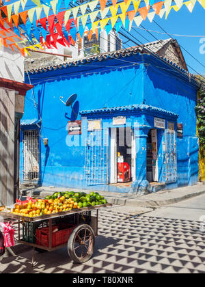 Bandiere colorate, edificio blu e frutta carrello su un angolo di strada nel Getsemani barrio, Cartagena, Colombia, Sud America Foto Stock