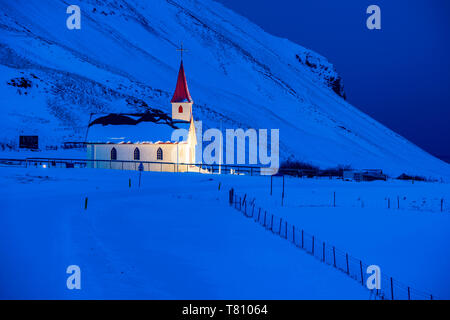 Chiesa illuminata all'alba contro montagne coperte di neve, vicino a VIK, Sud Islanda, Islanda, regioni polari Foto Stock