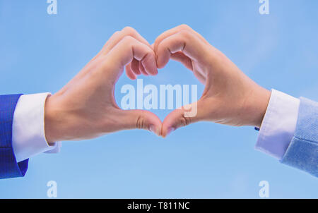 Le mani di mettere assieme in forma di cuore cielo blu sullo sfondo. Lato cuore gesto forme forma utilizzando le dita. Mani maschio a forma di cuore simbolo del gesto di amore e romanticismo. Amore il concetto di simbolo. Foto Stock