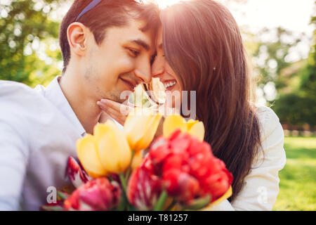 Felice coppia giovane in amore abbracciando con molla bouquet di fiori all'esterno. L'uomo dotato della sua fidanzata con i tulipani Foto Stock
