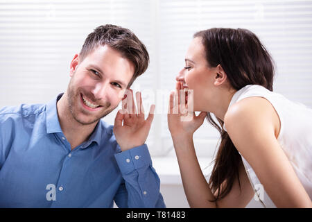 Ritratto di donna felice Whispering segreto o interessante Gossip all uomo bello nel suo orecchio Foto Stock