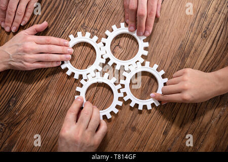 Un gruppo di imprenditori di unire insieme ingranaggi sul tavolo di legno al posto di lavoro Foto Stock