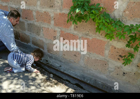 Yerevan, Nerkin Charbakh, Armenia, 03 Aprile 2014:un ragazzino impedisce a suo padre dalla pulizia della canaletta presso il recinto di pietra che vogliono aiutare lui Foto Stock