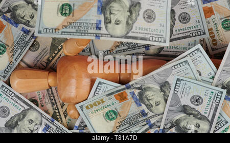 Uomo di Legno tenere 100 dollari sul mucchio di denaro lo sfondo Foto Stock