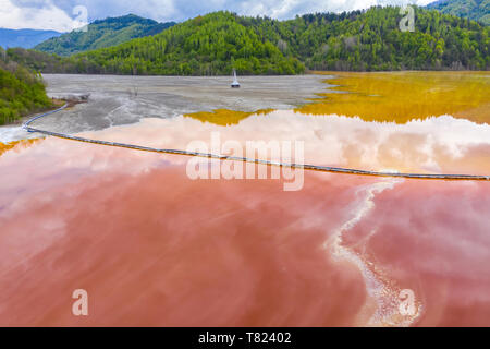 Vista aerea del data mining bacino di sedimentazione e la calce e alimentazione. Colorato di rosso profanato la mia acqua dal rame fossa aperta scavo in Geamana Rosia Montana, Roma Foto Stock