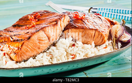 Gourmet o alla griglia da forno piccante di filetti di salmone con peperoncino rosso su un letto di riso servito con cipolle arrosto in una vista ravvicinata per un menu pubblicità Foto Stock