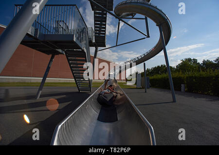 Kids godendo della splendida e grande slitta in metallo in corrispondenza di un parco giochi in un parco accanto al Vitra Design Museum di Weil am Rhein in estate sole Foto Stock